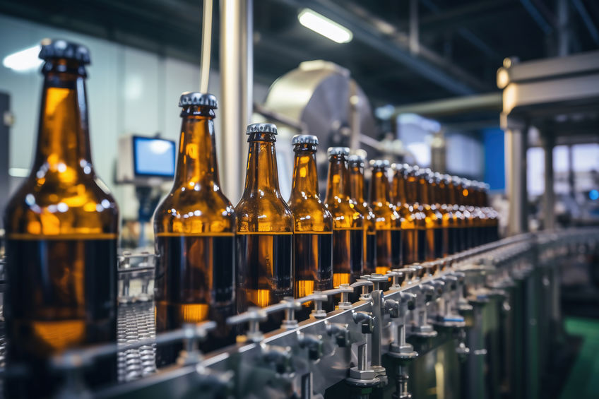 Brown glass bottles on an automated conveyor belt in a beverage bottling factory.
