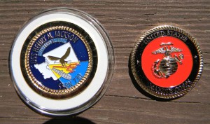 Two commemorative coins are placed on a wooden surface. The left coin features a blue background with an eagle design and text, while the right coin displays the United States Marine Corps emblem on a red background.